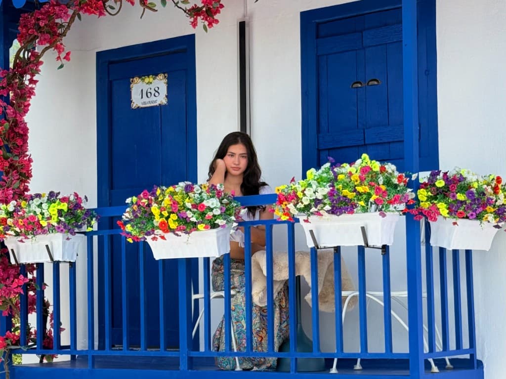 Villa balcony scene with bright blue doors and colorful flower boxes.
