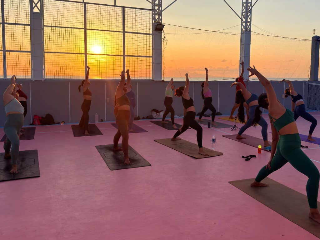 Group yoga session at sunset on an outdoor court with ocean horizon.